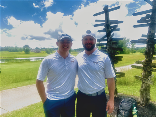 Boston Howard and Coach Ryan S. posing together in front of large green area and pond. 